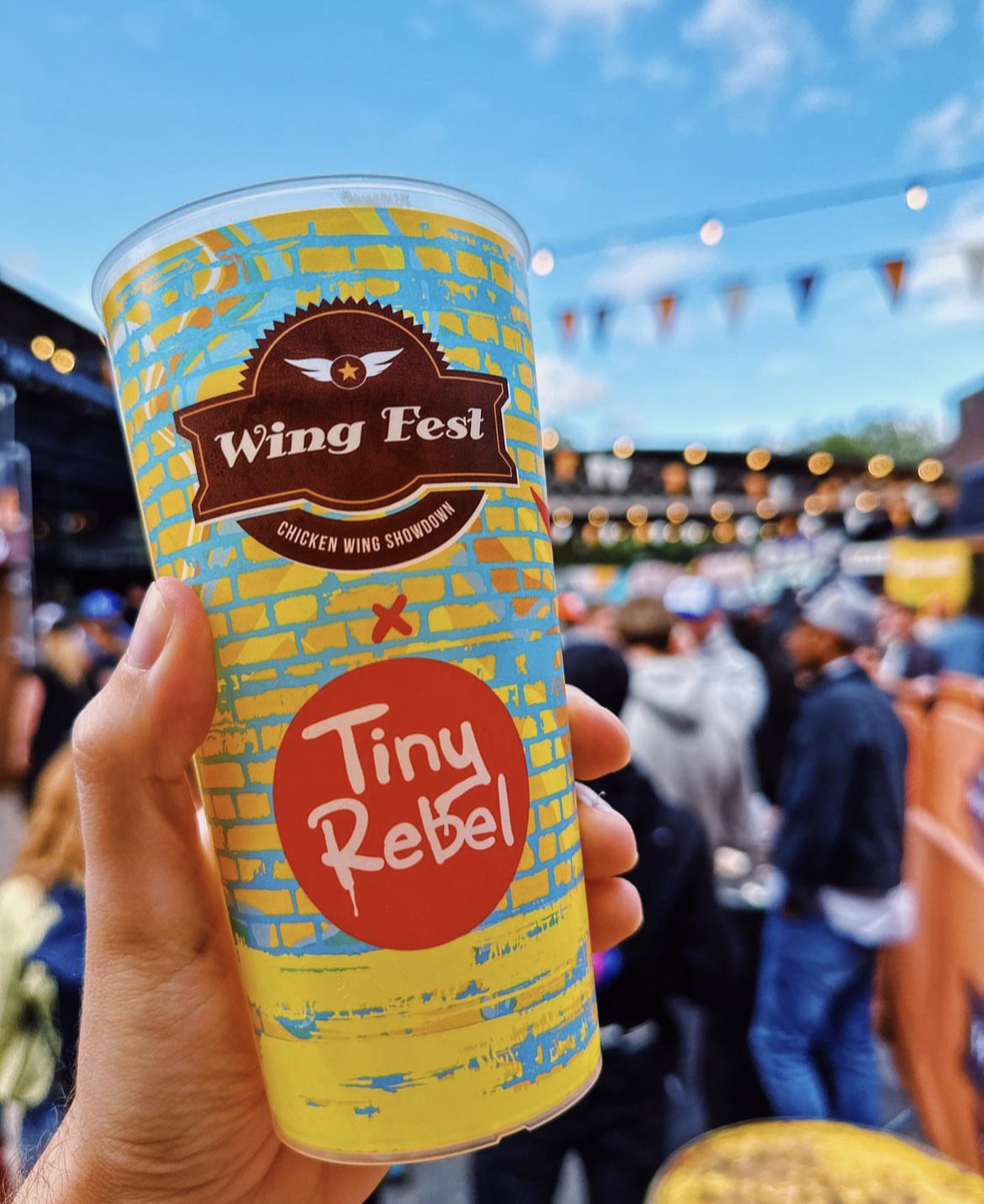 A full-colour branded reusable festival cup held up at an outdoor food festival