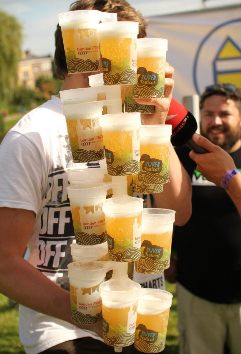 A festival worker holding a tall stack of branded reusable beer cups at an outdoor festival